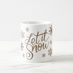 a white coffee mug with the words let it snow on it and snowflakes