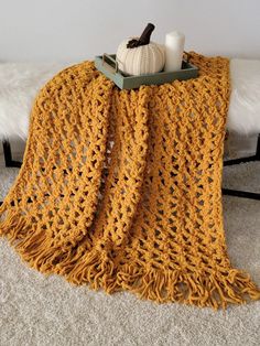 a yellow crocheted blanket sitting on top of a white rug next to a candle