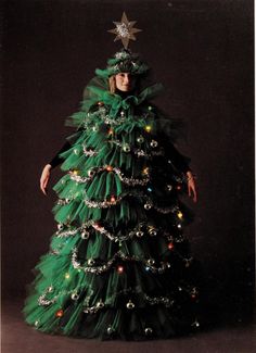 a woman in a green dress standing next to a christmas tree with lights on it