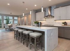 a large kitchen with marble counter tops and stools in front of an island that's surrounded by gray cabinets