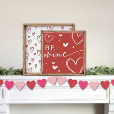 two framed valentine's day cards sitting on top of a mantel with garland