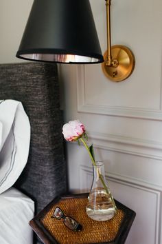 a flower in a vase on a table next to a lamp and eyeglasses