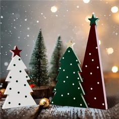 three paper christmas trees sitting on top of a wooden table with lights in the background