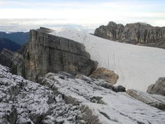 the snow is covering the rocks on the side of the mountain and there are mountains in the background