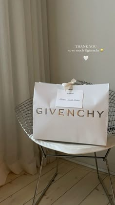 a white bag sitting on top of a chair in front of a window with the word givenchy written on it