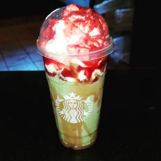 a starbucks drink with whipped cream and strawberries in it sitting on a black table