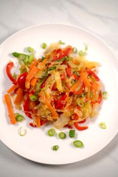 a white plate topped with vegetables on top of a table next to green onions and carrots