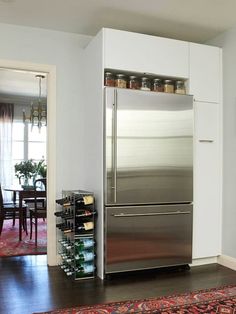 a stainless steel refrigerator and wine rack in a room with white walls, hardwood flooring and red rug