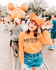 a woman in an orange shirt and denim shorts is posing for the camera with balloons behind her