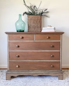 a wooden dresser sitting on top of a rug next to a vase with flowers in it