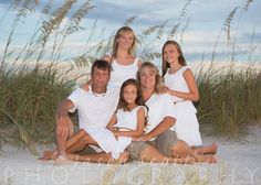 a family sitting on the beach in front of some tall grass