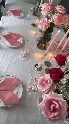 the table is set with pink napkins and flowers in vases, plates and candles