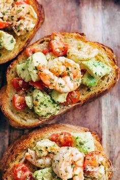 three pieces of bread with shrimp and tomatoes on them, sitting on a wooden surface