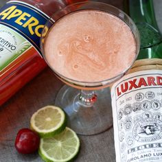 a bottle of liquor next to a glass filled with liquid and limes on a table