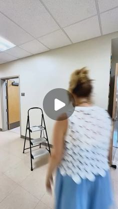 a woman in a blue dress walking through a room with white walls and tile floors