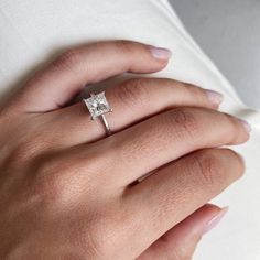 a woman's hand with a diamond ring on her left hand, wearing a white shirt