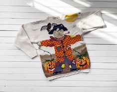 a white sweater with an image of a scarecrow on it and pumpkins in the background