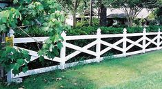 a white picket fence in the middle of a green yard with trees and bushes behind it