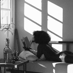 a woman sitting on a couch reading a book in front of a window with sunlight streaming through the windows