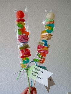 a person holding up some candy sticks with candies on them and a sign that says have a sweet summer