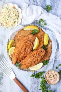 fried chicken on a plate with lemon wedges, coleslaw and parsley