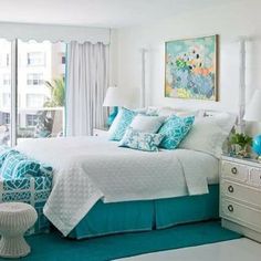 a bedroom with blue and white bedding, windows, and artwork on the wall