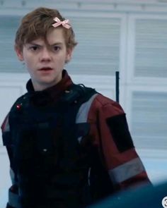 a young man wearing a red and black jacket standing in front of a garage door