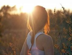 a woman standing in front of the sun with her back turned to the camera and looking into the distance