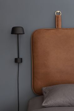 a bed with a brown leather headboard next to a black lamp and gray wall