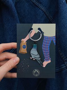 a person holding up a card with a bird on it's back and a dog keychain hanging from the front