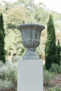 a large vase sitting on top of a white pedestal in the middle of a garden