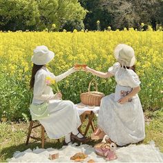 two women sitting on a blanket in front of a field with yellow flowers and bread