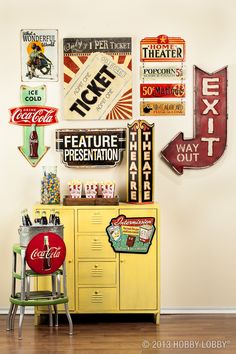 a yellow cabinet with coca - cola signs on the wall next to two stools