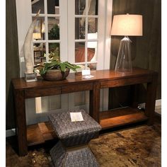 a wooden table with a glass vase on it and a plant in front of the window