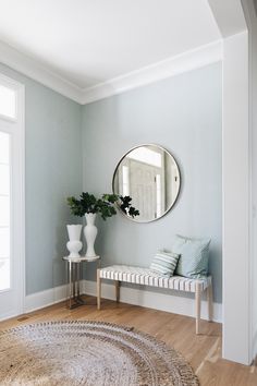 a room with a bench, mirror and vase on the wall