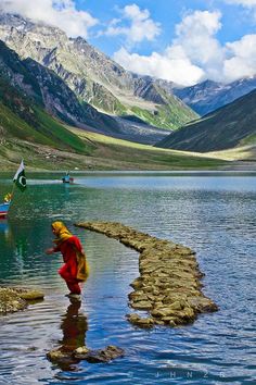 there is a woman that is standing in the water near mountains and rocks on the shore