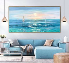 a living room with a blue couch and painting on the wall above it that has sailboats in the ocean