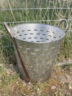 an old metal bucket sitting in the grass with a wooden spoon sticking out of it