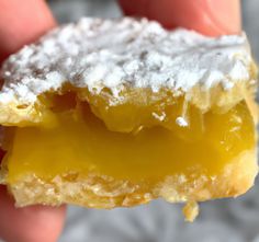 a close up of a person's hand holding a pastry with powdered sugar on top