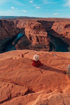 a person sitting on top of a large rock with a hat over their head in the desert