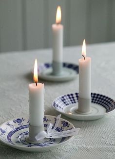 two white candles are on plates with blue and white designs