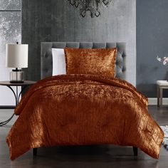 a bed with an orange velvet comforter and pillows on top of it, next to a chandelier