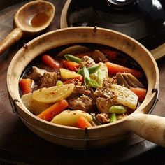 a wooden bowl filled with meat and veggies on top of a table next to spoons