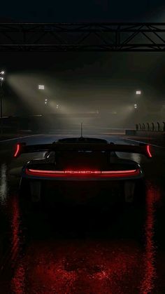 the rear end of a sports car with its lights on at night in a darkened area