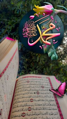 an open book sitting on top of a table next to a pink butterfly and green leaves