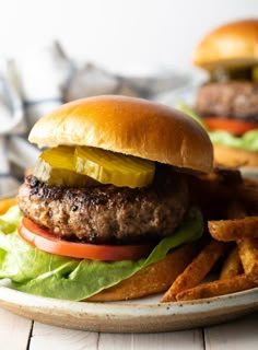 a hamburger with lettuce, pickles and tomatoes on a plate next to some fries