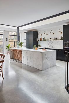 an open kitchen with marble counter tops and black cabinets, along with bar stools