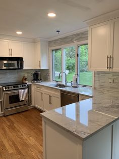 a kitchen with white cabinets and marble counter tops, stainless steel appliances and an open window