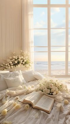 an open book on a bed with flowers and books in front of the window overlooking the ocean