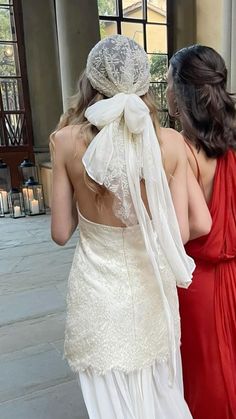 two women in dresses are walking down the street with veils on their heads and one is wearing a red dress